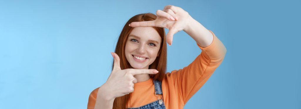 Creative good-looking nice redhead female assistant searching inspiration make hand frame look through delighted smiling satisfied found great spot take shot standing blue background