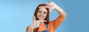 Creative good-looking nice redhead female assistant searching inspiration make hand frame look through delighted smiling satisfied found great spot take shot standing blue background