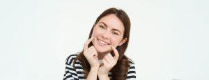 Portrait of attractive young woman with white, healthy smile, touches her dimples and looks happy. Concept of dental clinic and stomatology