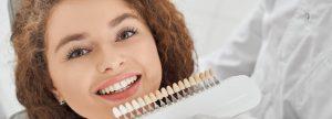Woman smiling while male dentist keeping teeth color range